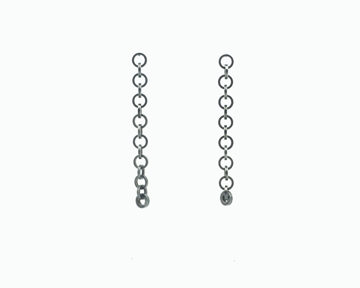 Zu sehen ist hier ein hängendes Ohrschmuck-Paar. Es sind zwei mit der Vorderseite nach vorne zeigende und nach unten hängende Kettenstücke aus ineinander eingehängten Kreisringelementen mit Vierkantprofil. Der Ohrschmuck ist anthrazitfarben. Er ist aus Edelstahl, Ruthenium geschwärzt.