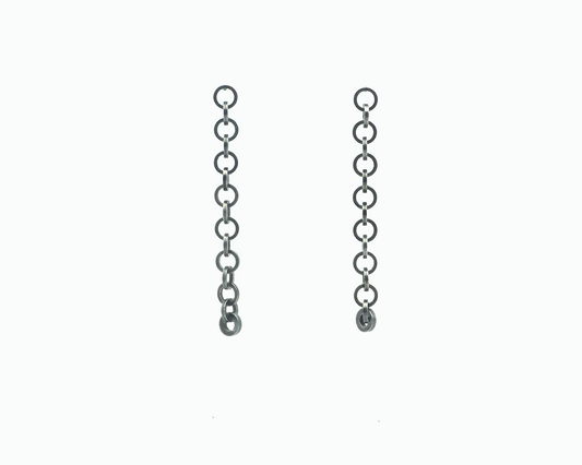 Zu sehen ist hier ein hängendes Ohrschmuck-Paar. Es sind zwei mit der Vorderseite nach vorne zeigende und nach unten hängende Kettenstücke aus ineinander eingehängten Kreisringelementen mit Vierkantprofil. Der Ohrschmuck ist anthrazitfarben. Er ist aus Edelstahl, Ruthenium geschwärzt.
