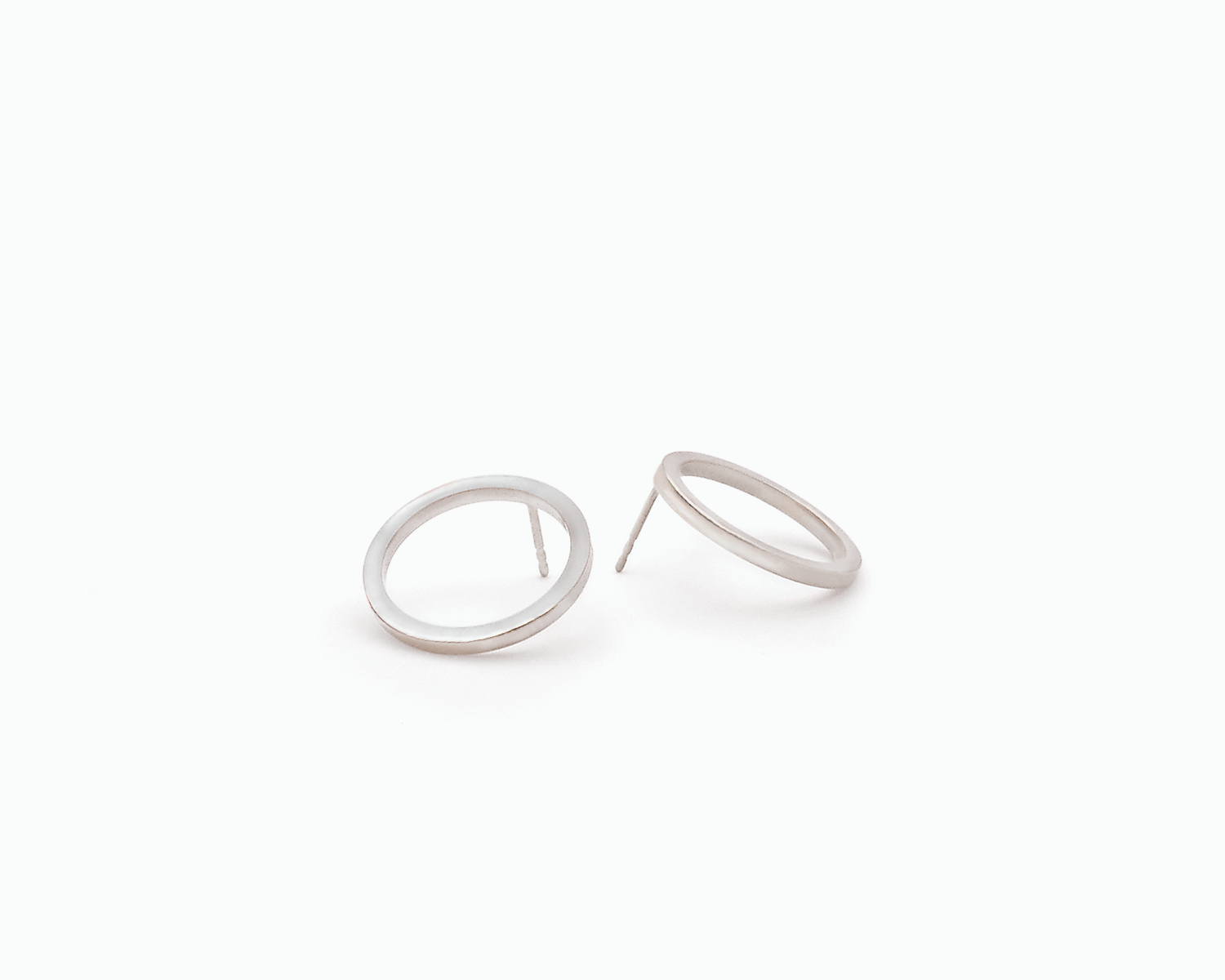 Zu sehen ist hier ein Ohrschmuck-Paar. Es sind zwei in unterschiedlicher Perspektive liegende, circa münzgroße, kreisförmige Ringe mit Vierkantprofil, an deren Rückseiten jeweils der Steckerstift sitzt. Der Ohrschmuck ist silberfarben. Er ist aus Edelstahl, Silber plattiert.