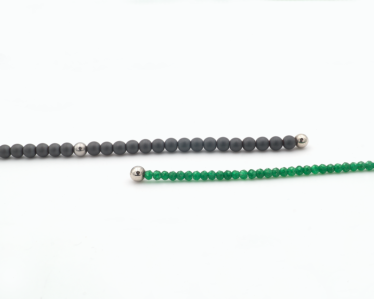 Dies ist ein Detailbild mit offenen, sich überlappenden Kettenenden. Der hintere Kettenstrang ist ein Ausschnitt der einen Kettenseite mit Hämatitkugeln, der vordere Kettenstrang zeigt die andere Kettenseite mit Grünachatkugeln.