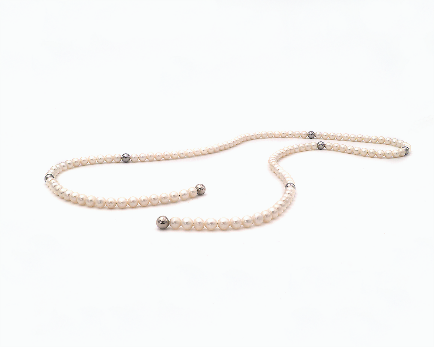 Zu sehen ist hier eine Kette aus weißer Süßwasserperle. Dazwischen sitzen Edelstahlkugeln und an den Enden Magnetkugeln. Die Kette ist offen und leicht kurvig liegend dargestellt.