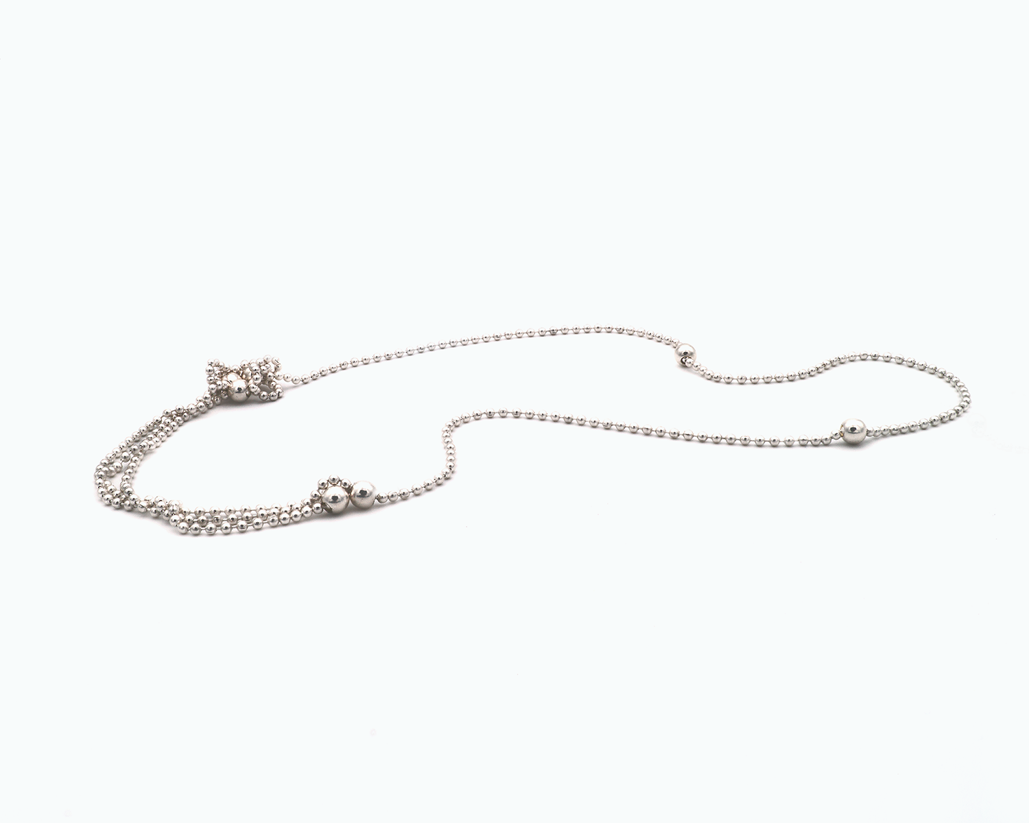 Zu sehen ist hier eine Kugelkette mit weiteren, vereinzelt integrierten größeren Kugeln. Die Kette ist liegend in einer Tragevariante dargestellt, bei der die Kette vorne im Dekolletébereich dreireihig liegt mit seitlich dickeren Abschnitten. Dies ist eine der vielen Trageoptionen dieser wandelbaren Kette. Die gesamte Kette ist silberfarben (Silber plattiert).