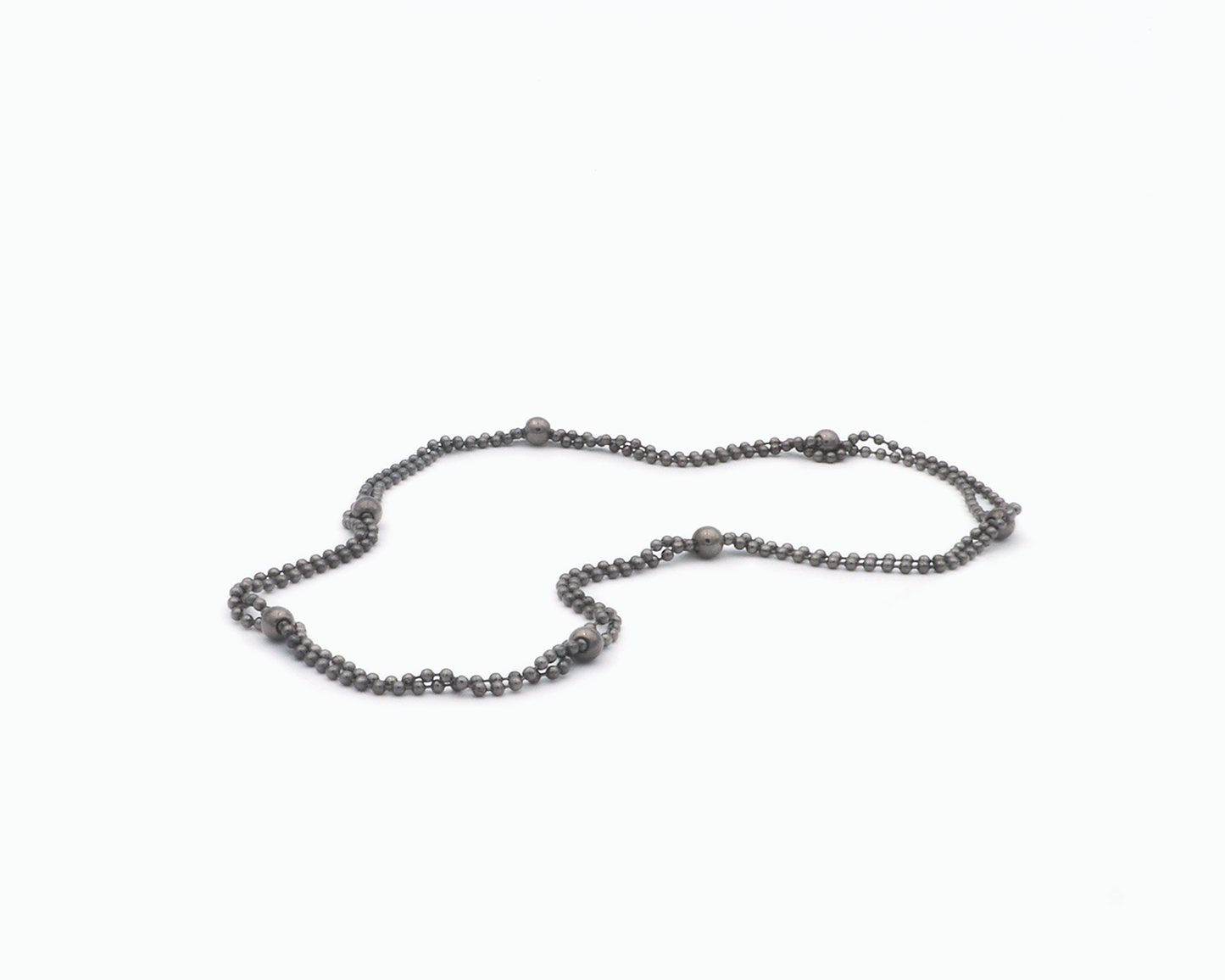 Zu sehen ist hier eine Kugelkette mit weiteren, vereinzelt integrierten größeren Kugeln. Die Kette ist hier doppelt gelegt drapiert, so dass sie wie eine kurze Kette aussieht. Dies ist eine der vielen Tragevarianten dieser wandelbaren Kette. Die gesamte Kette ist dunkel, anthrazitfarben (Ruthenium geschwärzt).