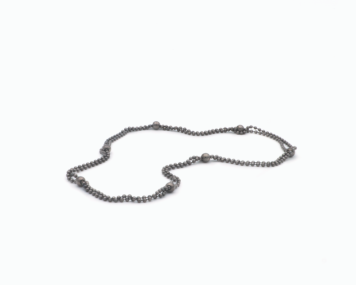 Zu sehen ist hier eine Kugelkette mit weiteren, vereinzelt integrierten größeren Kugeln. Die Kette ist hier doppelt gelegt drapiert, so dass sie wie eine kurze Kette aussieht. Dies ist eine der vielen Tragevarianten dieser wandelbaren Kette. Die gesamte Kette ist dunkel, anthrazitfarben (Ruthenium geschwärzt).