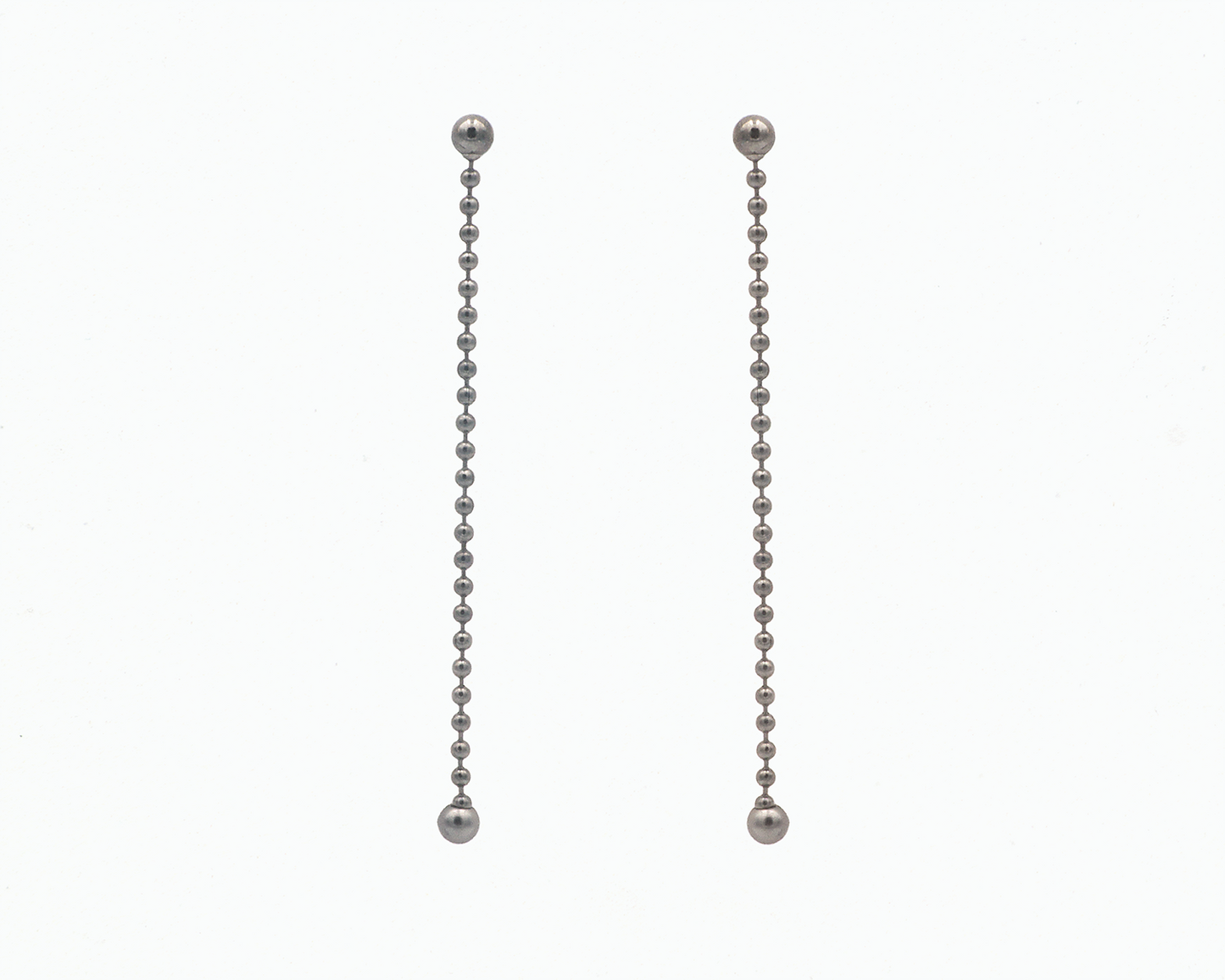 Zu sehen ist hier ein hängendes Ohrschmuck-Paar. Es sind zwei mit der Vorderseite nach vorne zeigende und nach unten hängende Kugelkettenstücke, an deren Abschluss unten jeweils eine größere Magnetkugel sitzt. Der Ohrschmuck ist anthrazitfarben. Er ist aus Edelstahl, Ruthenium geschwärzt.
