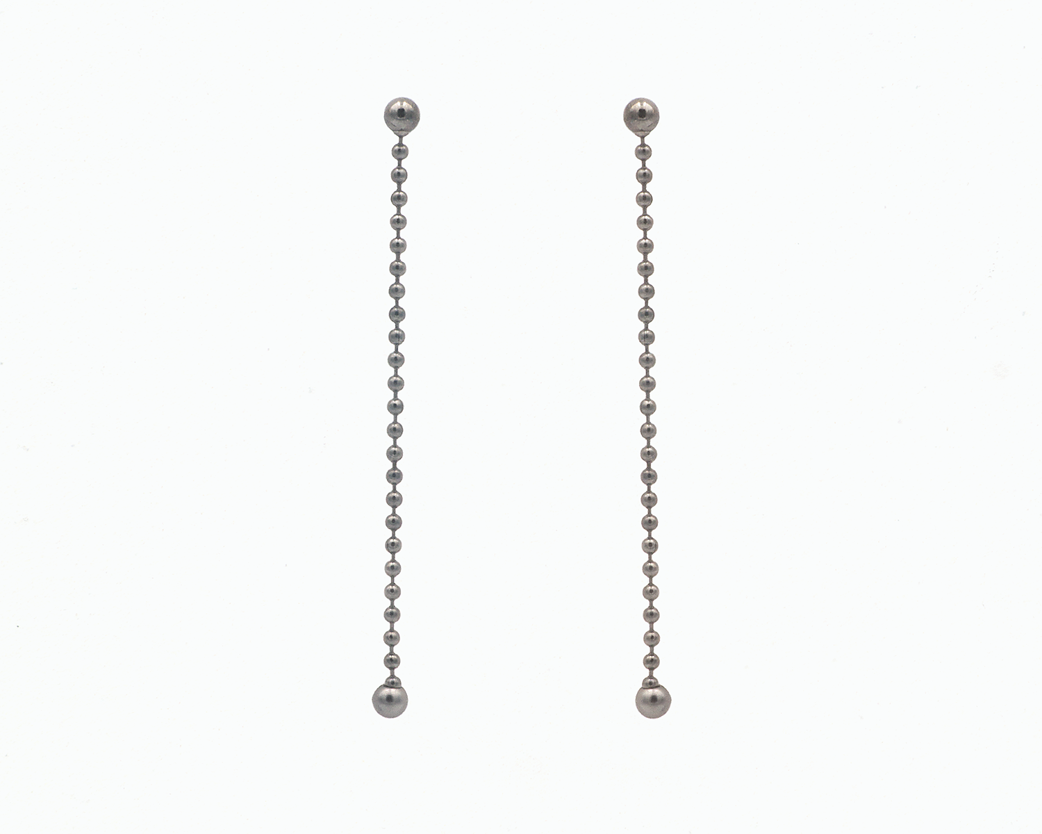 Zu sehen ist hier ein hängendes Ohrschmuck-Paar. Es sind zwei mit der Vorderseite nach vorne zeigende und nach unten hängende Kugelkettenstücke, an deren Abschluss unten jeweils eine größere Magnetkugel sitzt. Der Ohrschmuck ist anthrazitfarben. Er ist aus Edelstahl, Ruthenium geschwärzt.
