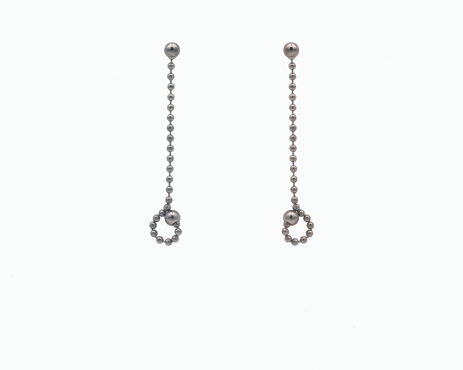 Zu sehen ist hier ein hängendes Ohrschmuck-Paar. Es sind zwei mit der Vorderseite nach vorne zeigende und nach unten hängende Kugelkettenstücke, an deren Enden unten jeweils ein Teil des Kettenstranges als kleine Schlaufe am dort sitzenden Magneten angedockt ist. Dies ist eine der vielen Tragemöglichkeiten dieses Ohrschmuckes. Der Ohrschmuck ist anthrazitfarben. Er ist aus Edelstahl, Ruthenium geschwärzt.