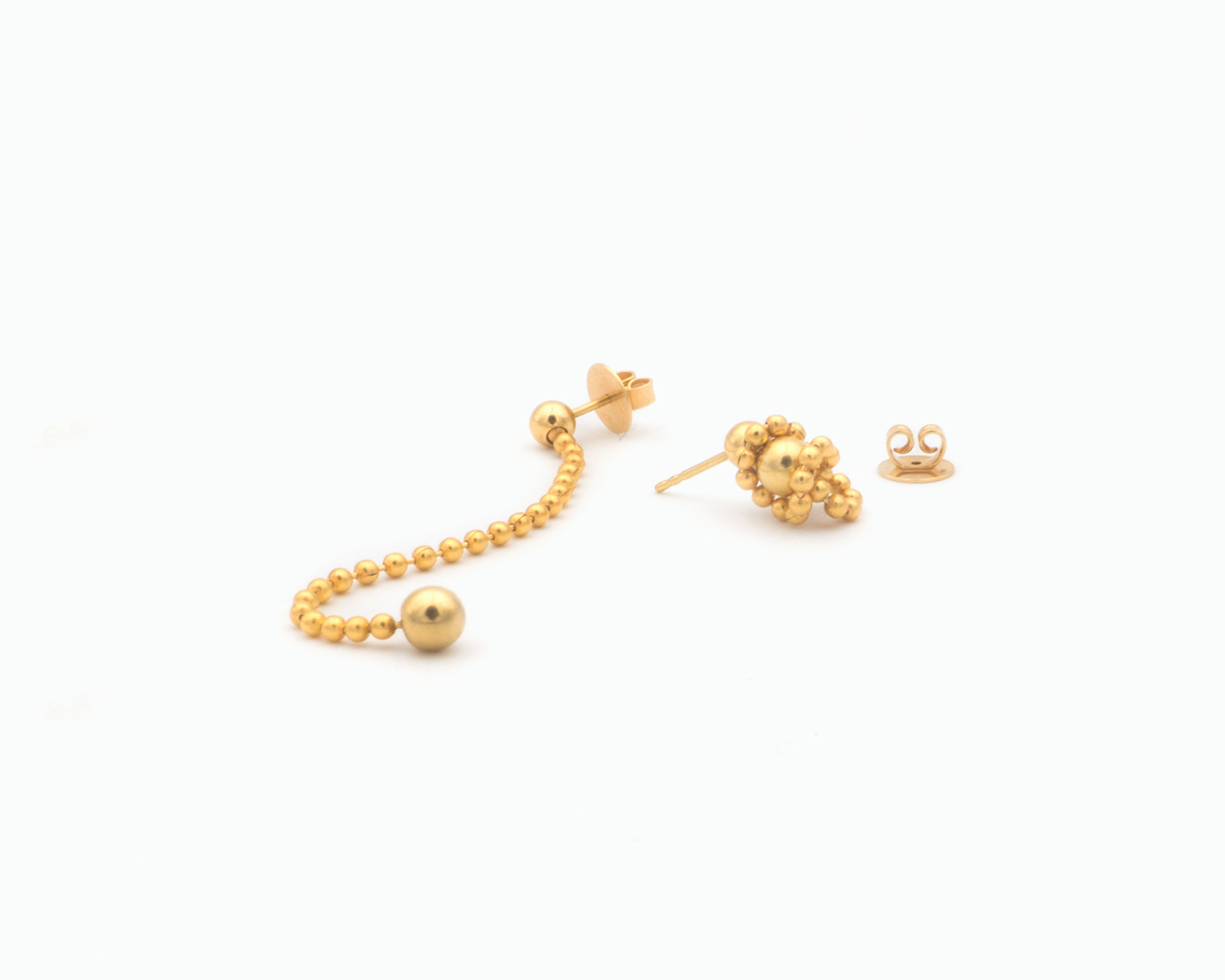 Zu sehen ist hier ein variabel tragbares Ohrschmuck-Paar. Beide Stecker sind aus unterschiedlicher Perspektive und in verschiedenen Tragevarianten gezeigt. Links ist ist Ohrstecker  lang liegend gezeigt und rechts als kurzer „Kettenknäuel“. Links ist der Rückstecker aufgesteckt und rechts liegt er daneben. Der Ohrschmuck ist goldfarben. Er ist aus Edelstahl, Feingold plattiert.