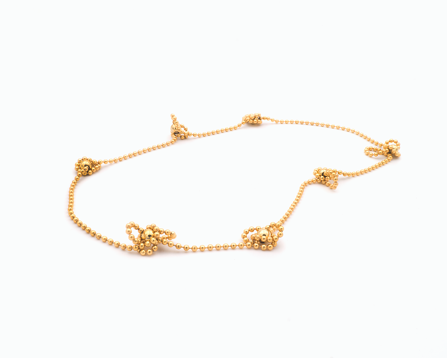 Zu sehen ist hier eine Kugelkette mit weiteren, vereinzelt integrierten größeren Kugeln. Die Kette ist hier mit vereinzelten kleinen vermeintlichen Knotenpunkten dargestellt. An diesen “Knotenpunkten“ tummeln sich Kettenabschnitte, da sie dort von den in der Kette eingearbeiteten Magnetkugeln angezogen werden. Dies ist eine der vielen Tragevarianten dieser wandelbaren Kette. Die gesamte Kette ist goldfarben (Feingold plattiert).