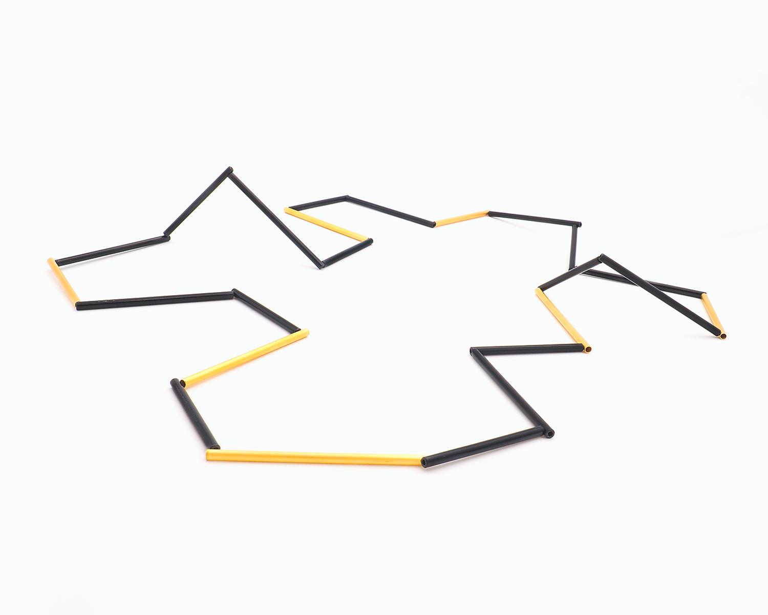 Zu sehen ist hier eine liegende Kette mit schwarzen und goldfarbenen Stäben. Die Stäbe sind Rohrabschnitte in zwei verschiedenen Längen. Die Kette hat eine grafische Anmutung, bei der die Linie als Hauptakteur dominiert.
