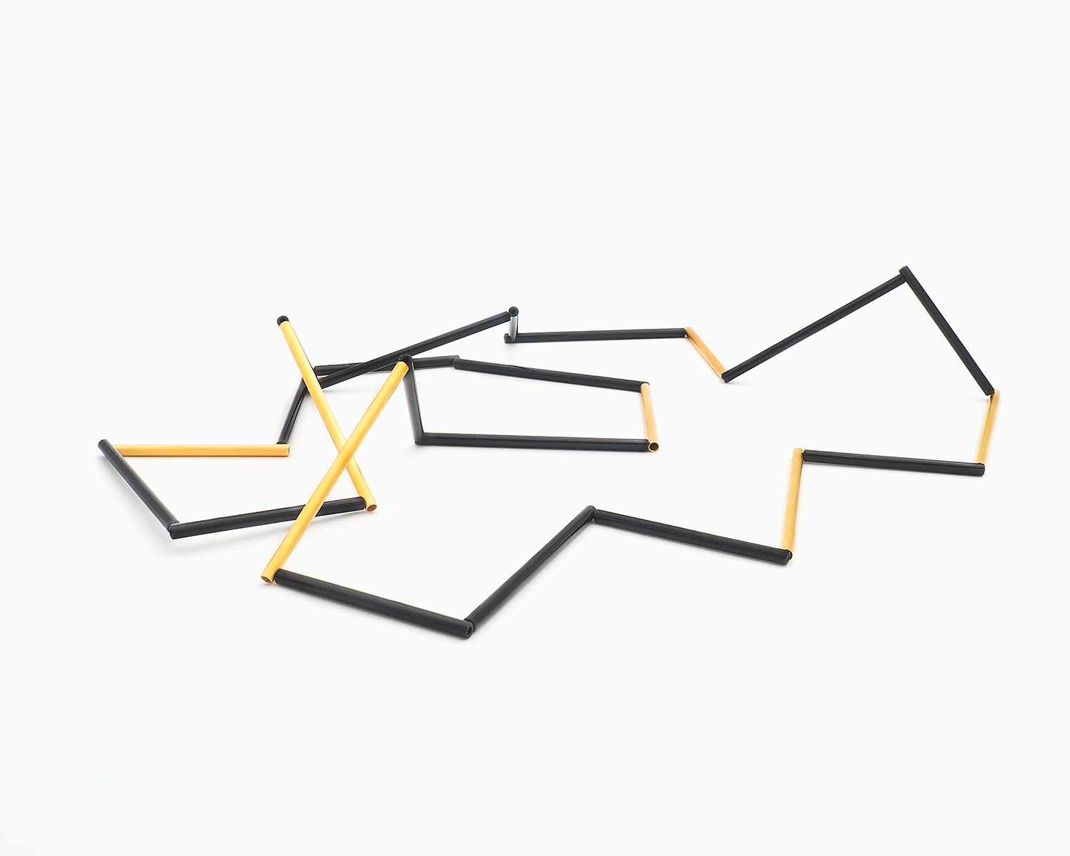 Zu sehen ist hier eine liegende Kette mit schwarzen und goldfarbenen Stäben. Die Stäbe sind Rohrabschnitte in zwei verschiedenen Längen. Die Kette hat eine grafische Anmutung, bei der die Linie als Hauptakteur dominiert.