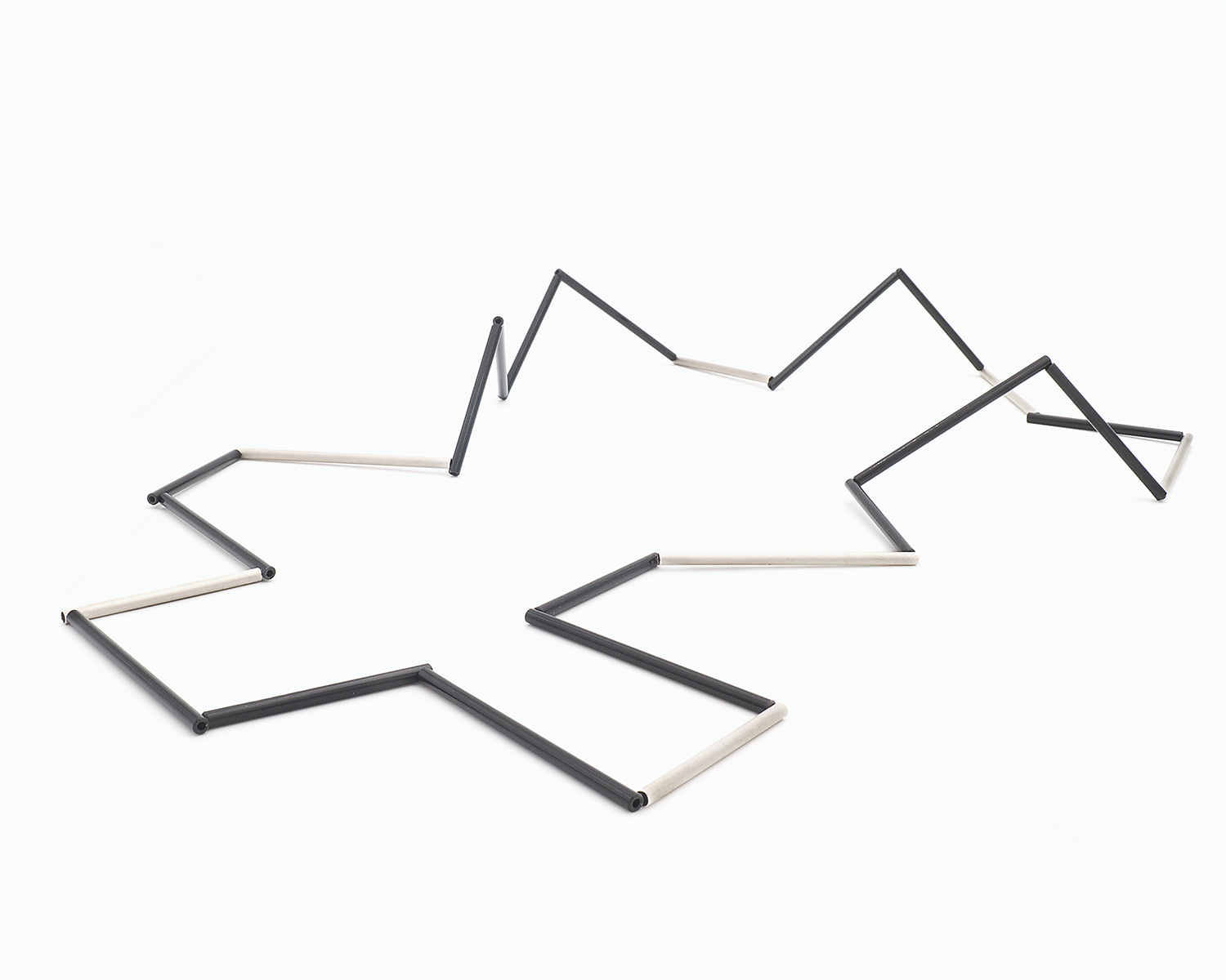 Zu sehen ist hier eine liegende Kette mit schwarzen und silbernen Stäben. Die Stäbe sind Rohrabschnitte in zwei verschiedenen Längen. Die Kette hat eine grafische Anmutung, bei der die Linie als Hauptakteur dominiert.