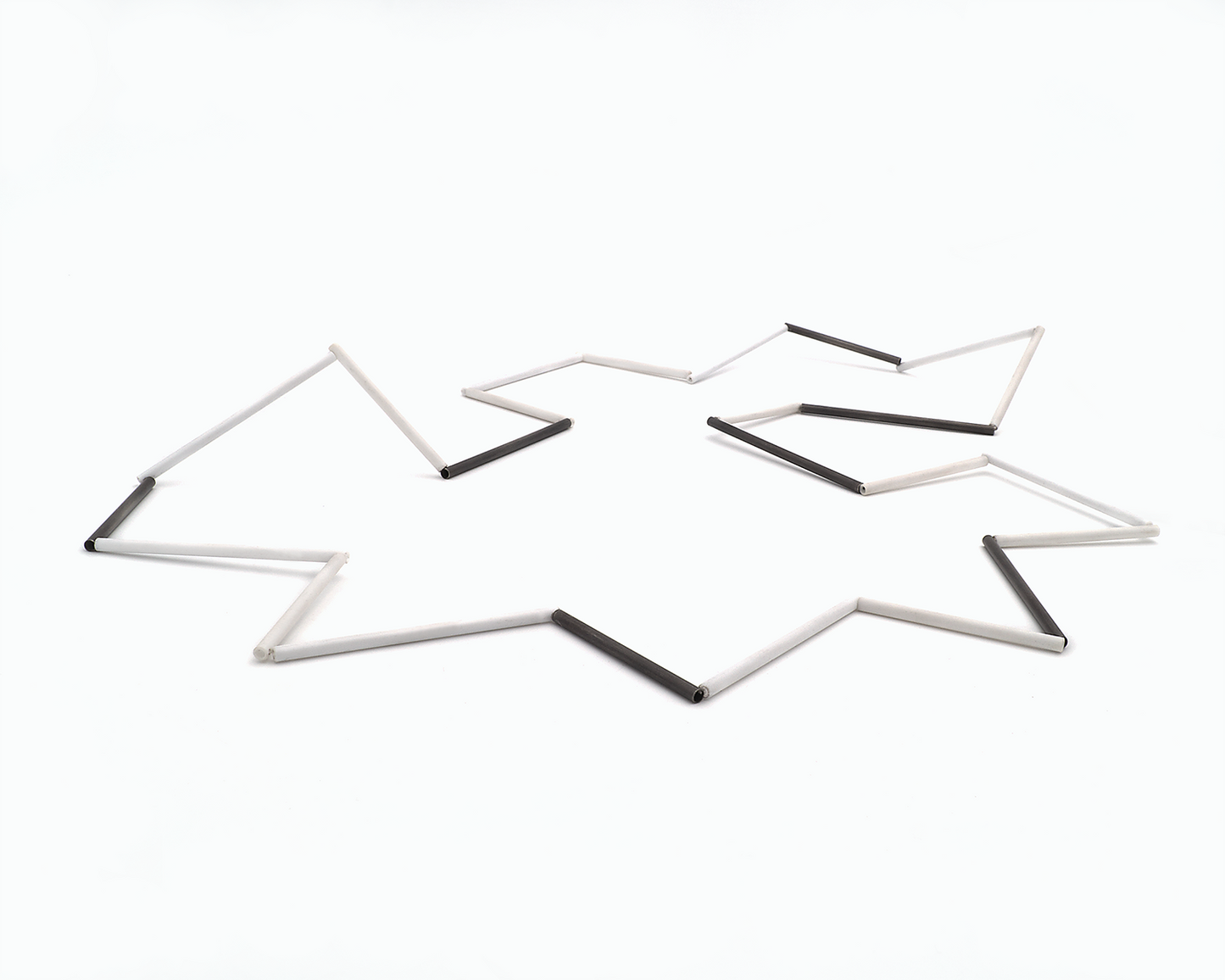 Zu sehen ist hier eine liegende Kette mit weißen und schwarzen Stäben. Die Stäbe sind Rohrabschnitte in zwei verschiedenen Längen. Die Kette hat eine grafische Anmutung, bei der die Linie als Hauptakteur dominiert.