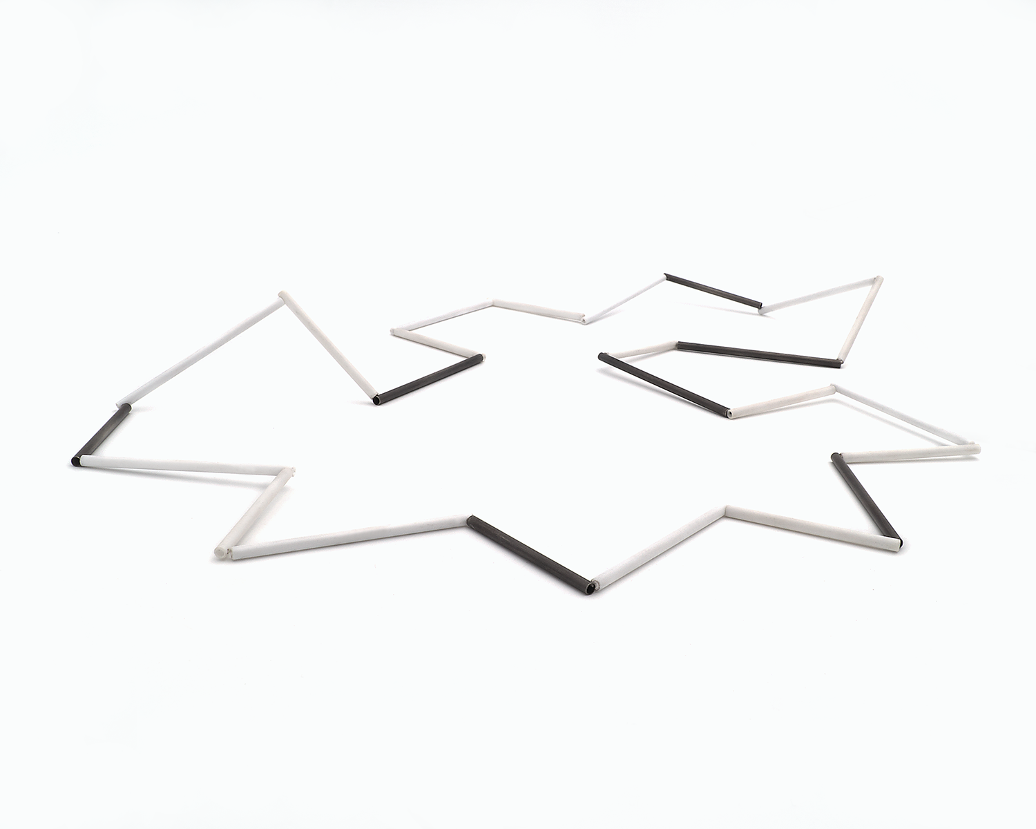 Zu sehen ist hier eine liegende Kette mit weißen und schwarzen Stäben. Die Stäbe sind Rohrabschnitte in zwei verschiedenen Längen. Die Kette hat eine grafische Anmutung, bei der die Linie als Hauptakteur dominiert.